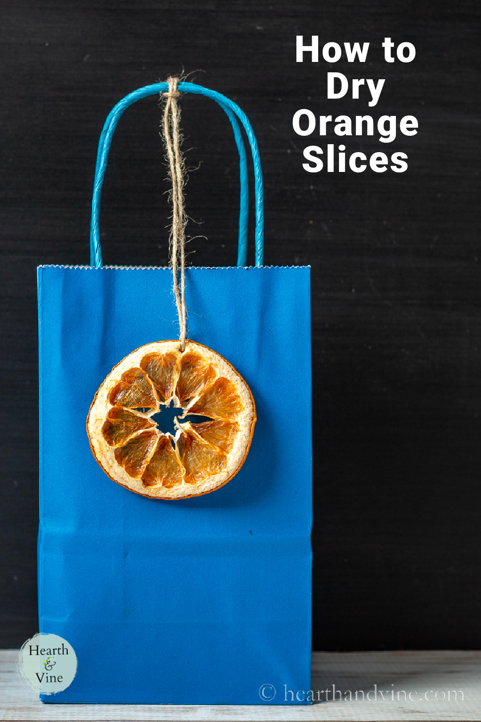 Small blue gift bag with a dried orange slice tag hanging from a piece of twine tied to the handle.