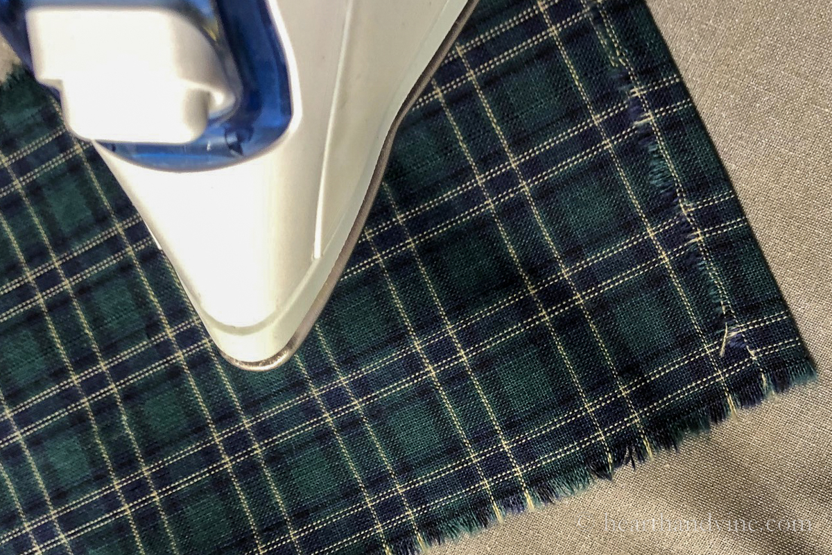 An iron pressing the edge of a blue and green plaid fabric.