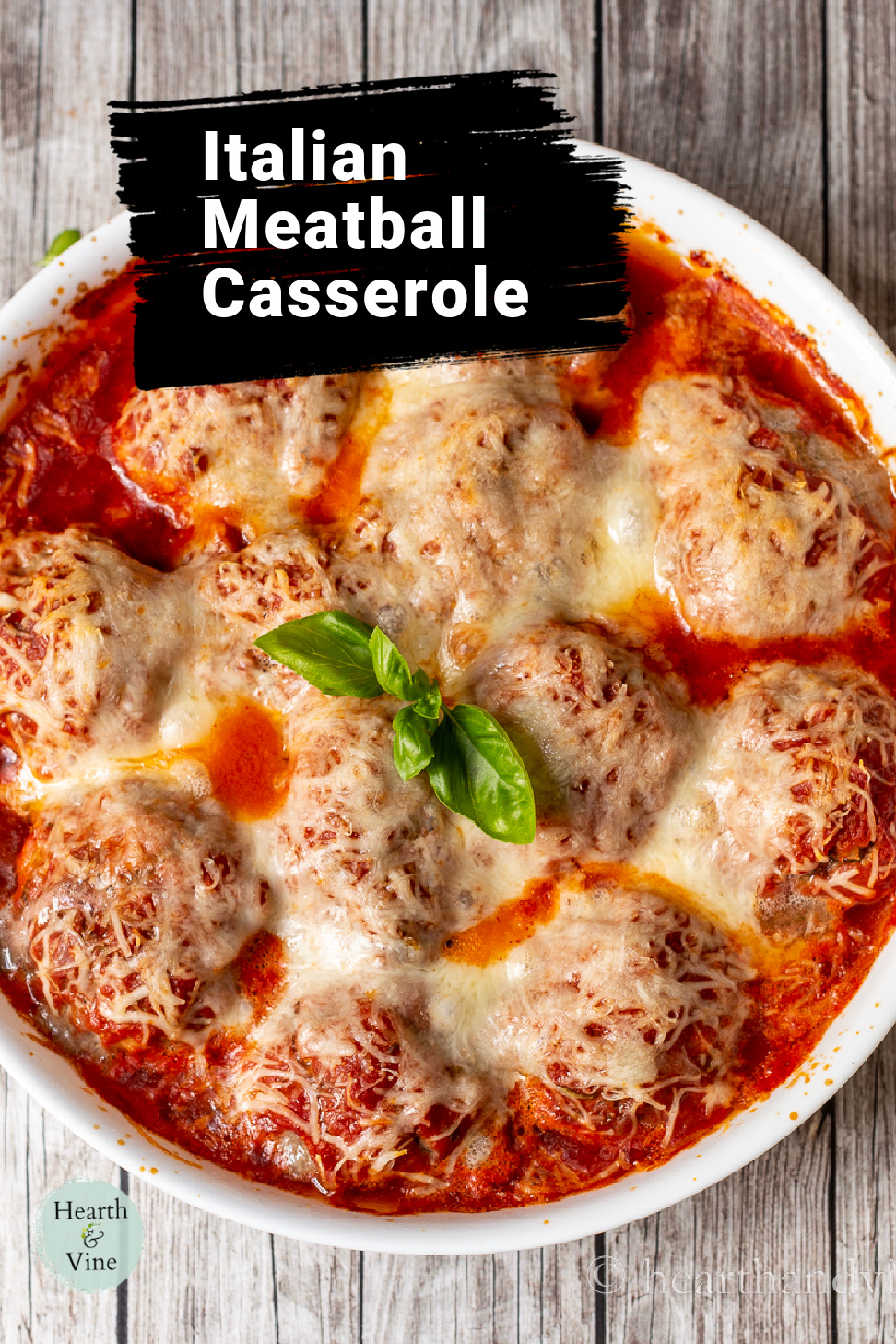 Meatball casserole in a white baking pan with a sprig of fresh basil in the center as garnish.