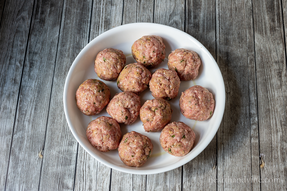 Twelve hand-rolled meatballs in a white round baking pan.
