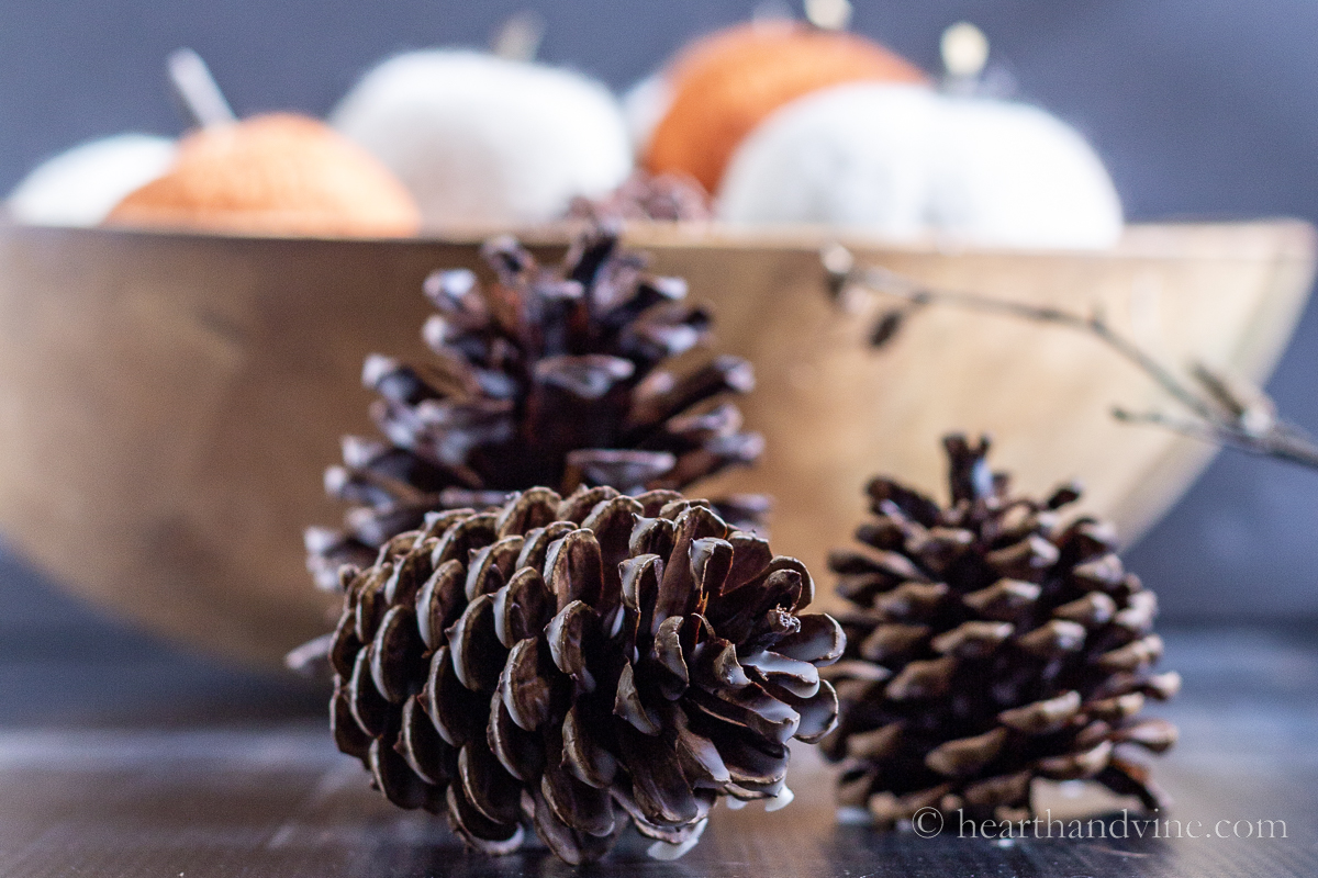 Three waxed scented pine cones in front of a dough bowl with felted pumpkins.