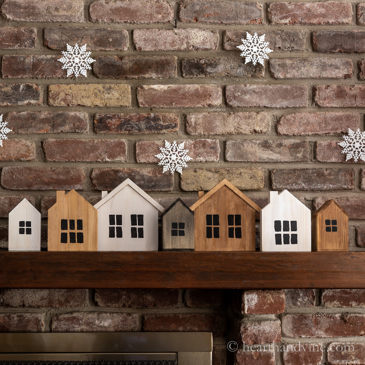 Close up of the center of the mantel showing painted wooden houses and snowflakes hanging from the trim molding.