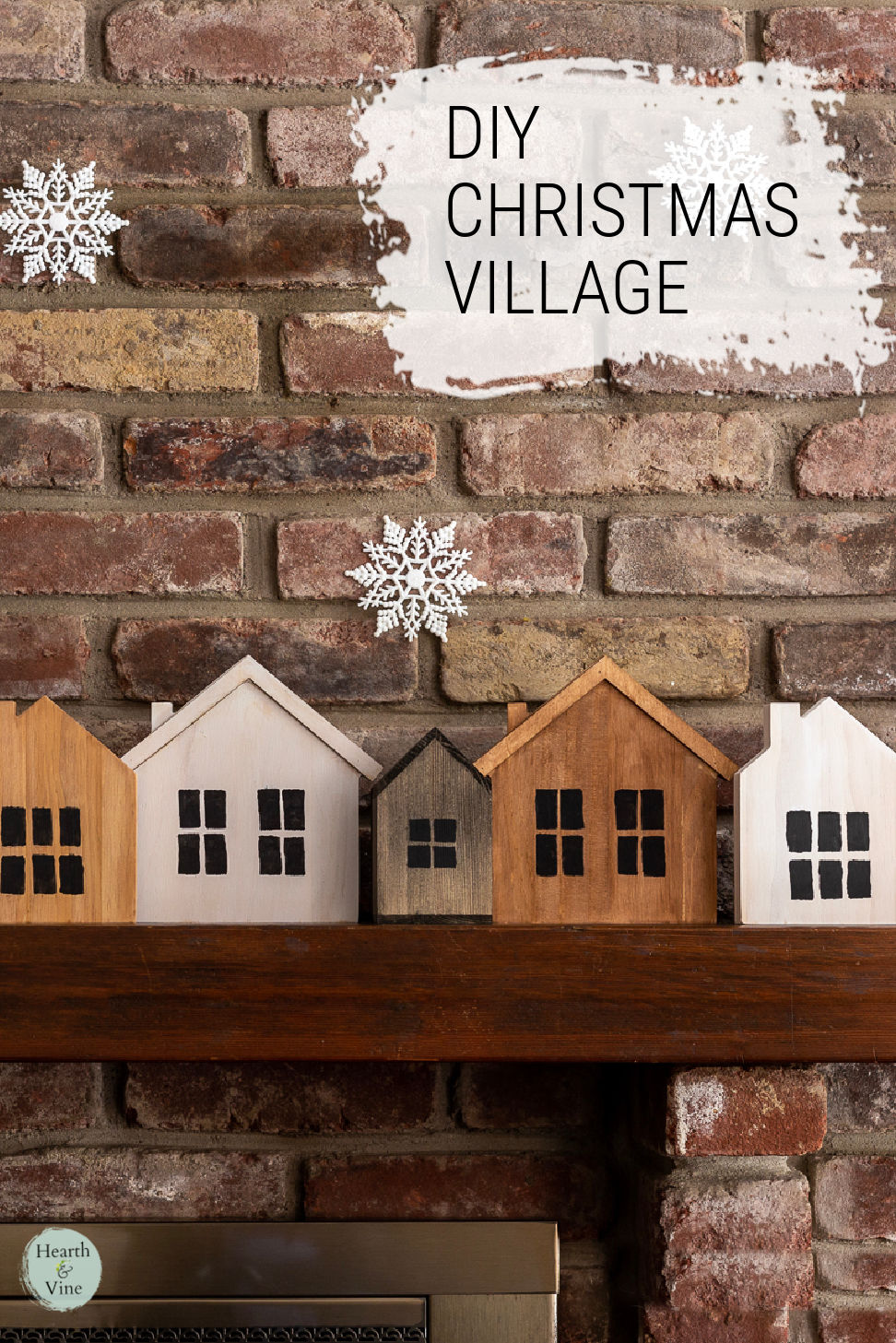 Wooden houses on mantel with snowflakes hanging from above.