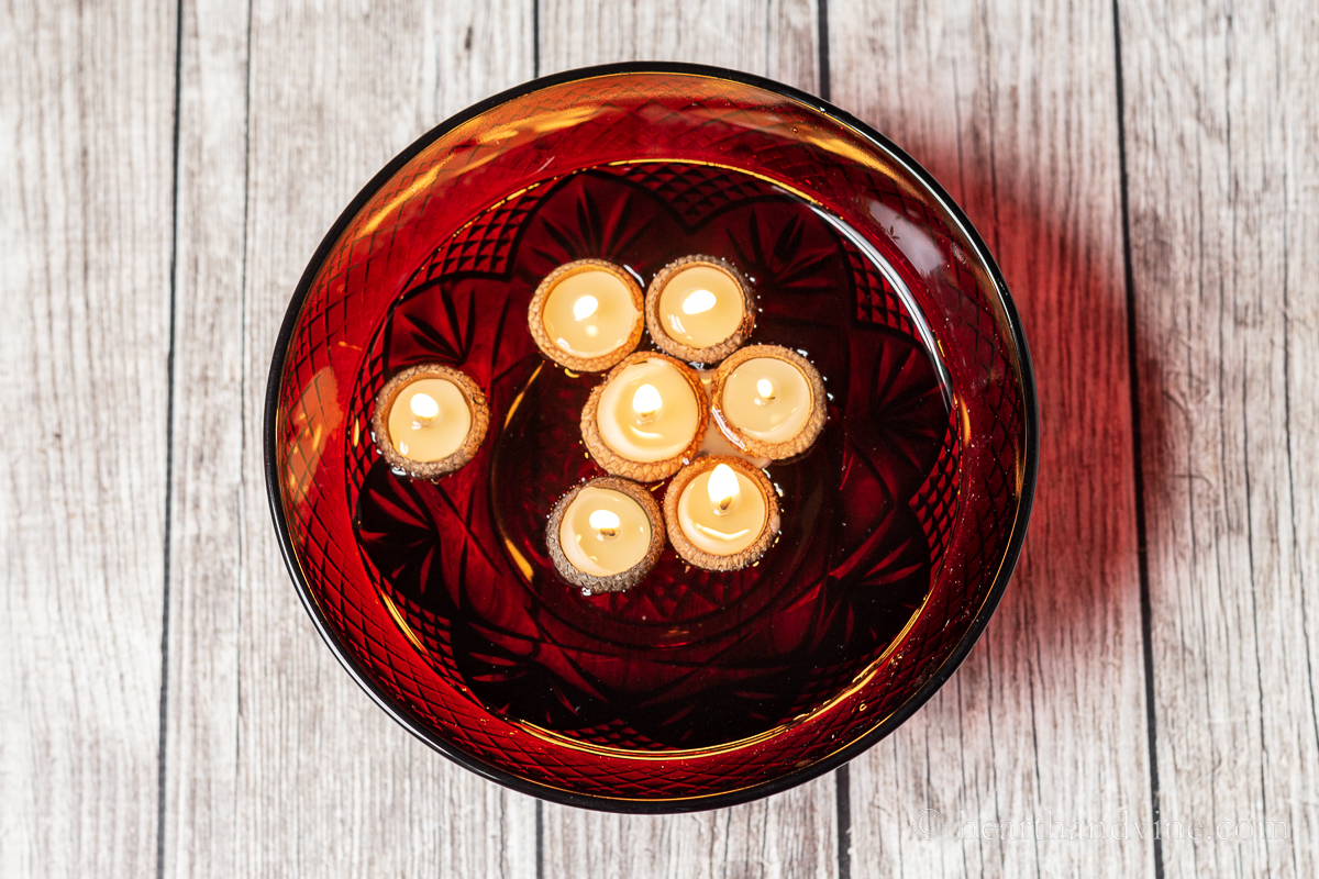 Beeswax acorn cap candles lit and floating in a bowl of water.