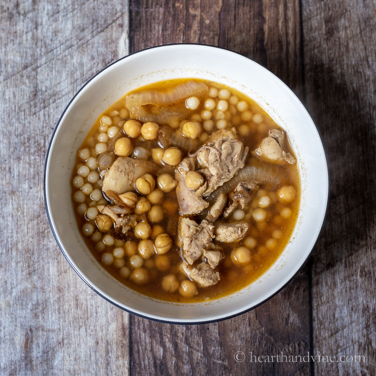 White serving bowl with Moghrabieh balls, chicken, broth, onions and chickpeas.