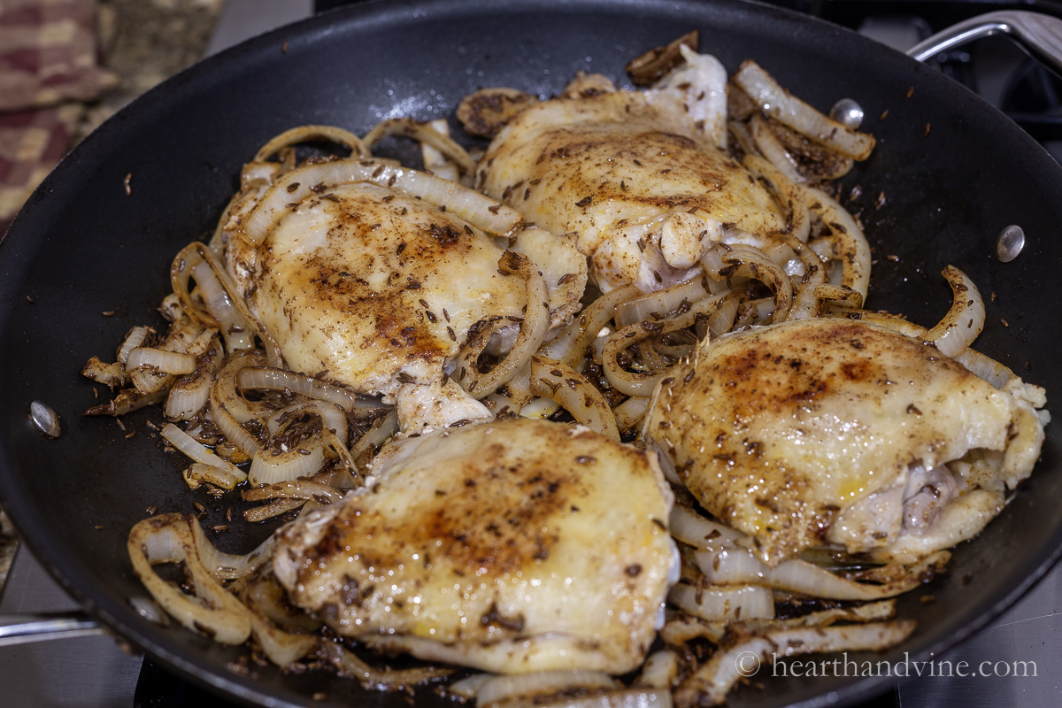 Chicken thighs with skin and bone browning in onion mixture.