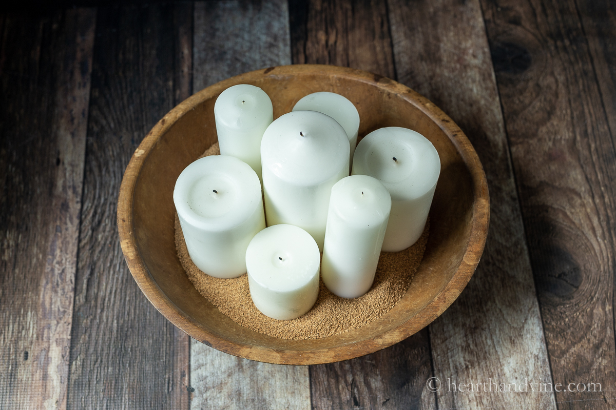 Different sized white pillar candles set in walnut shells in a vintage round dough bowl.