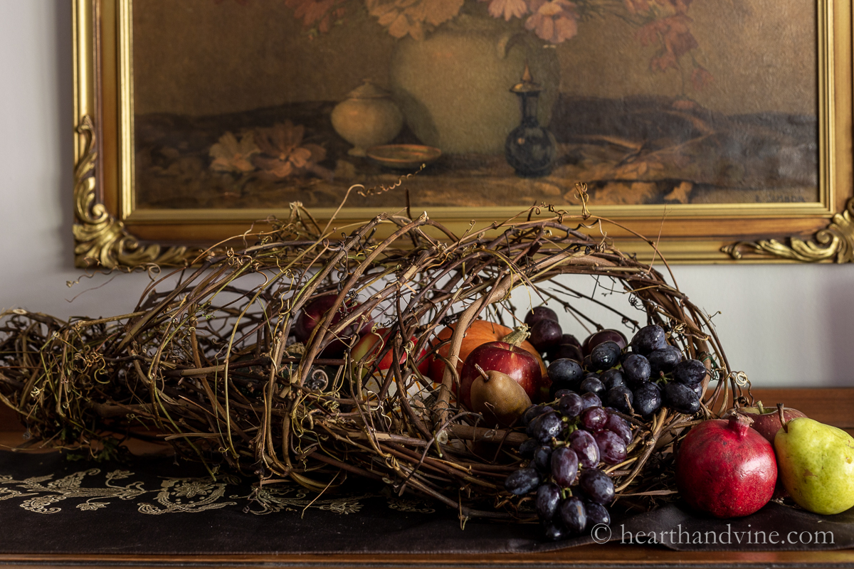 DIY cornucopia made from grapevines on a dining room buffet filled with fresh fruit.
