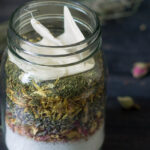 Mason jar layered with bath salts and herbs and a small muslin bag.