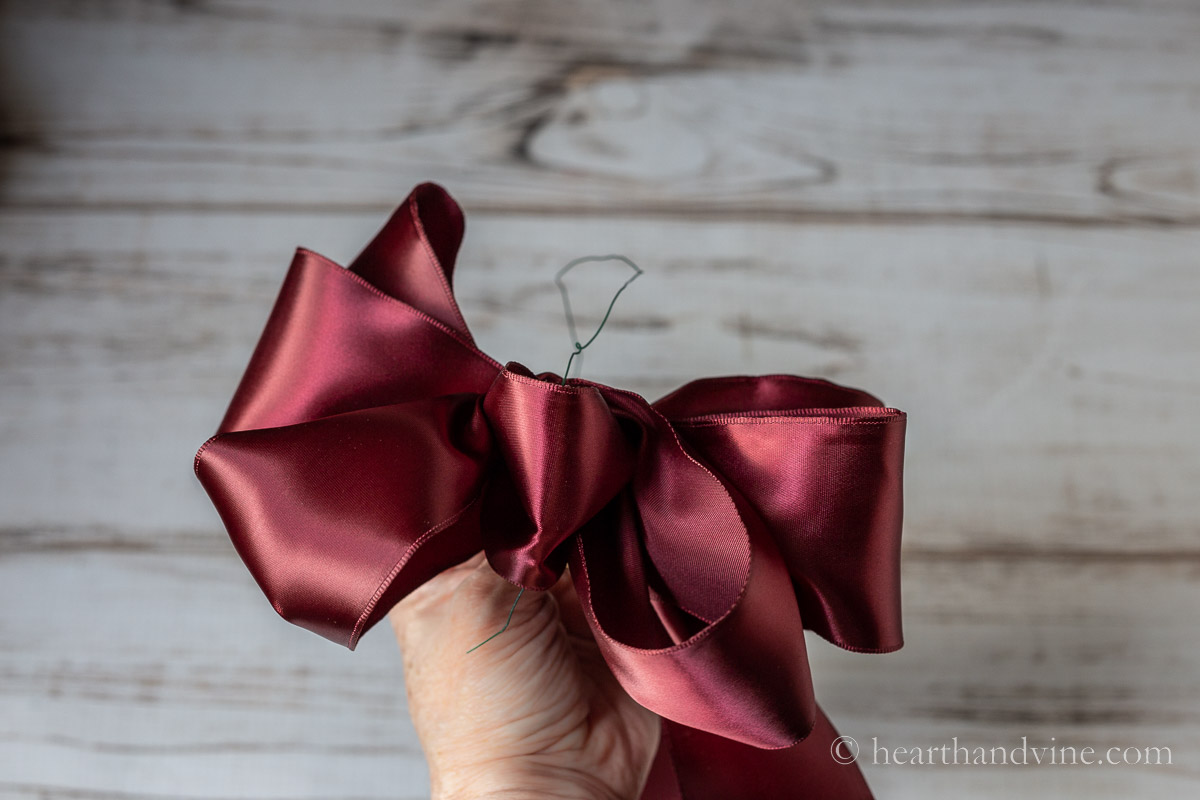 Adding a piece of wire to the back of a red bow.