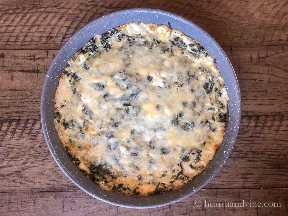 Cheesy spinach dip in a round baking pan fresh from the oven.