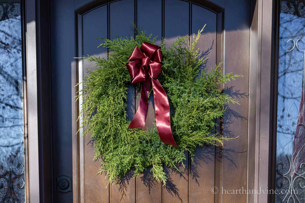 A large red satin bow on a fresh greens wreath hanging on the front door.
