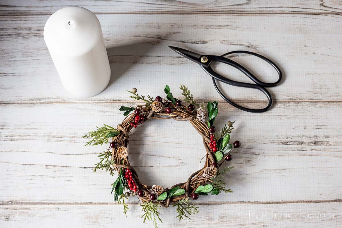 A white pillar candle, a pair of floral scissors and a Christmas candle ring.