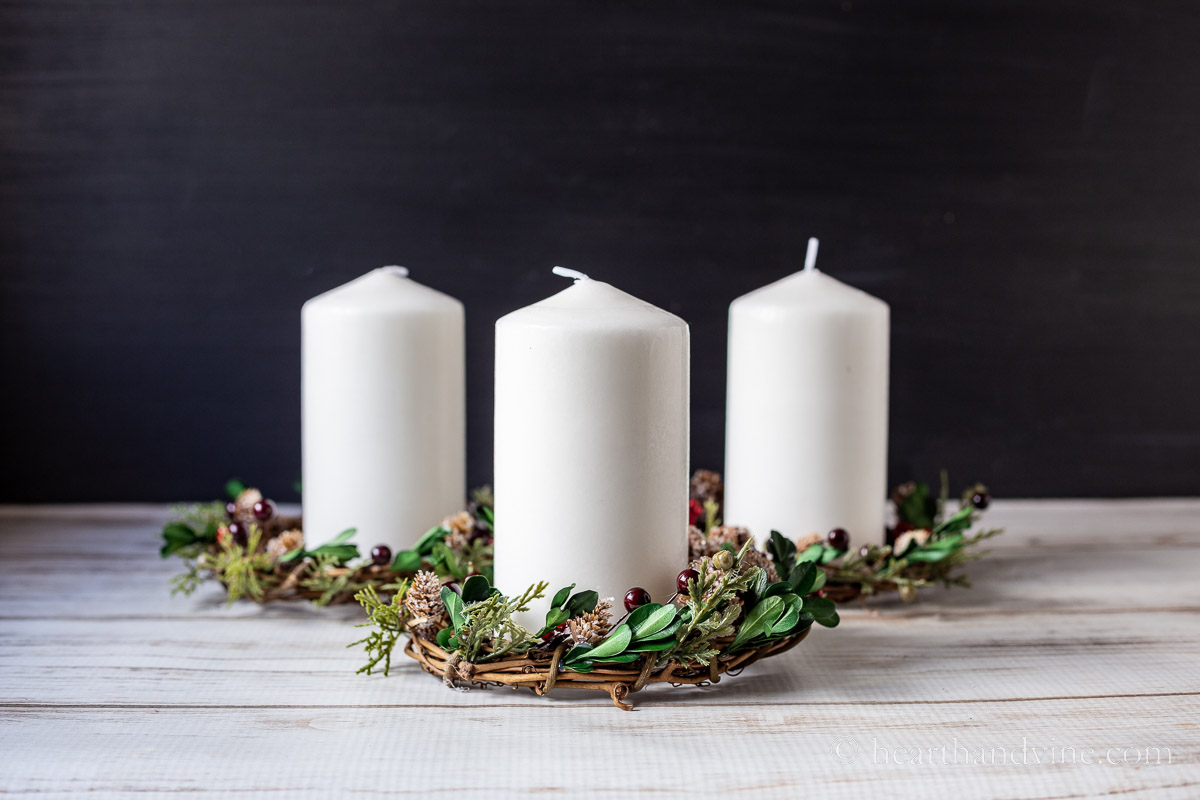 Three Christmas candle wreaths with white pillar candles inside.