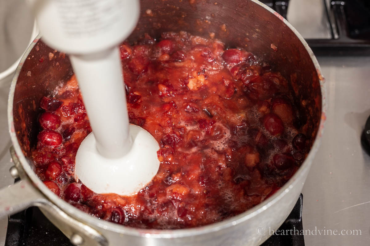 An immersion blender pureeing cranberries, spices and sugar in a saucepan.