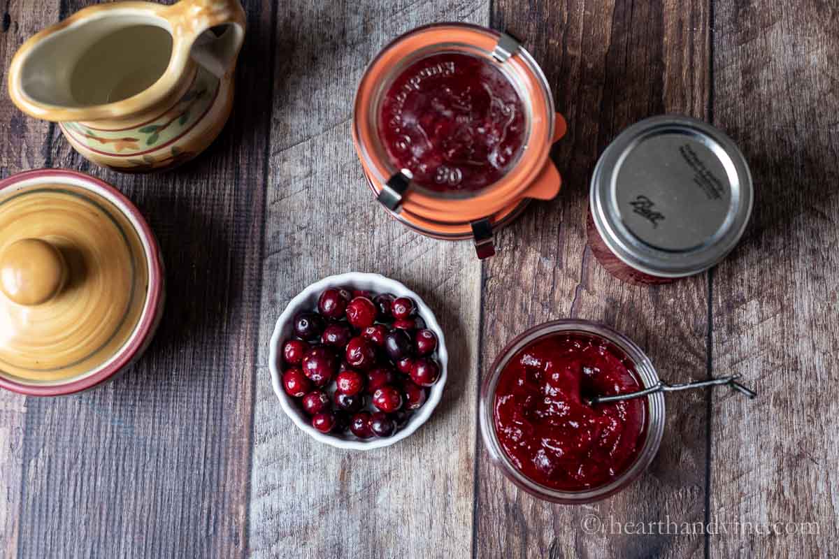 An aerial view of cranberries in a dish and an open jar of cranberry jam with a little spoon.