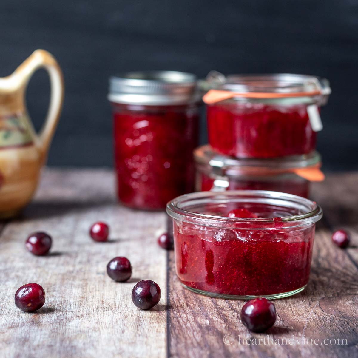 Jars of cranberry jam and fresh cranberries scattered on the table.