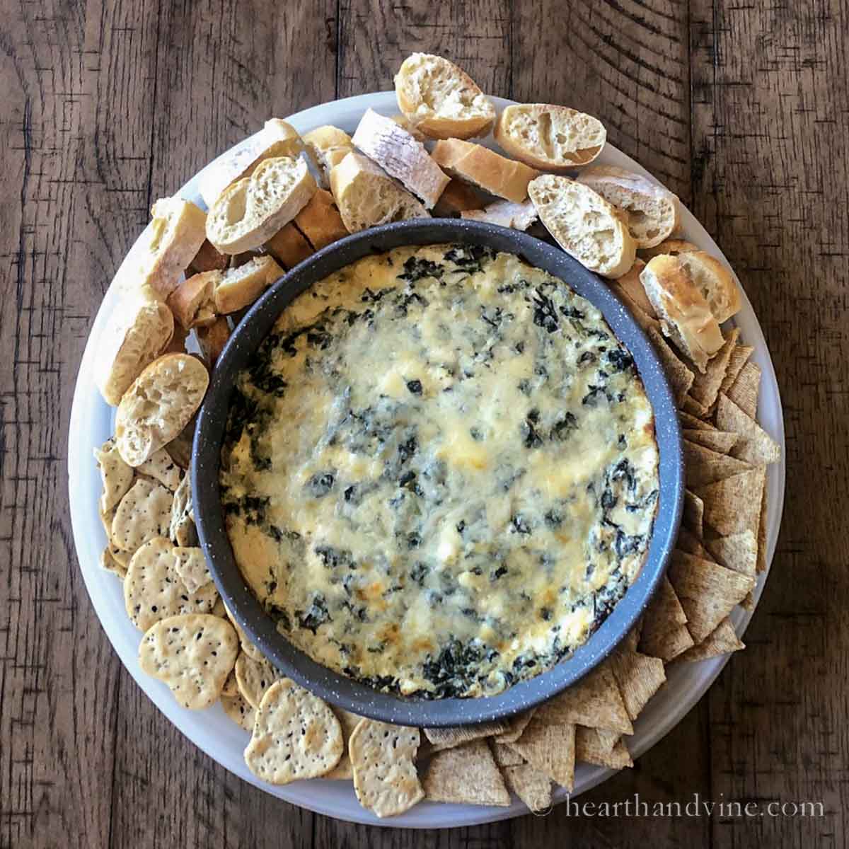 Spinach dip with cream cheese on a platter with crackers and slice baguette bread rounds.