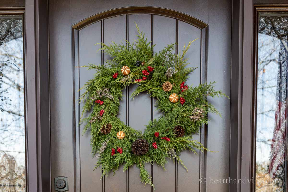 A decorated fresh evergreen wreath on a brown front door.