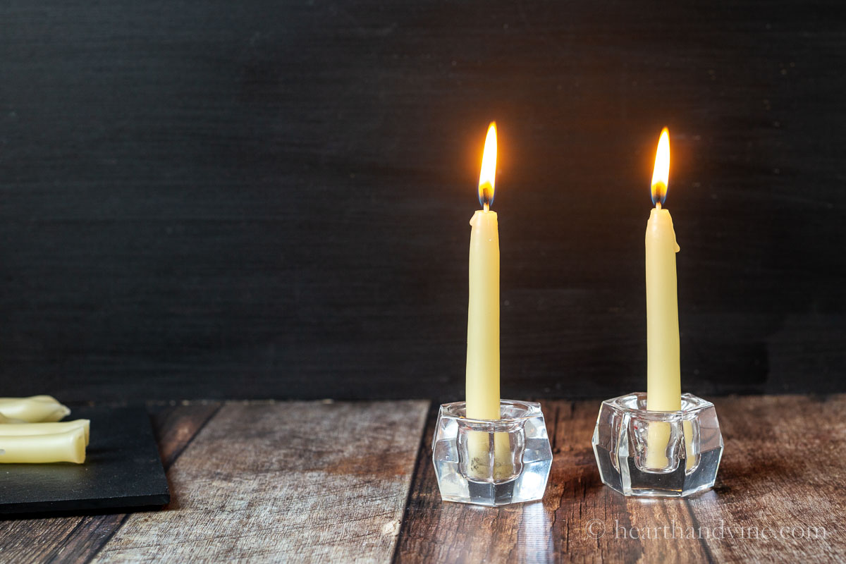 Two taper beeswax candles lit in small candle holders.