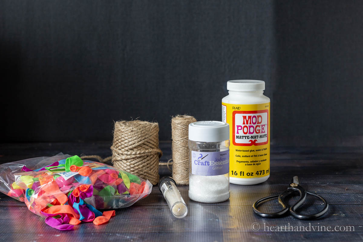 Supplies for twine ball ornaments including water balloons, twine, glitter, mod podge and scissors.