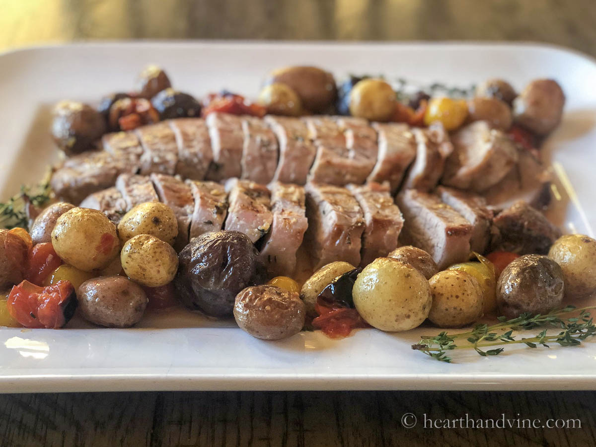 Platter with cooked pork tenderloin, mini potatoes, tomatoes and thyme.
