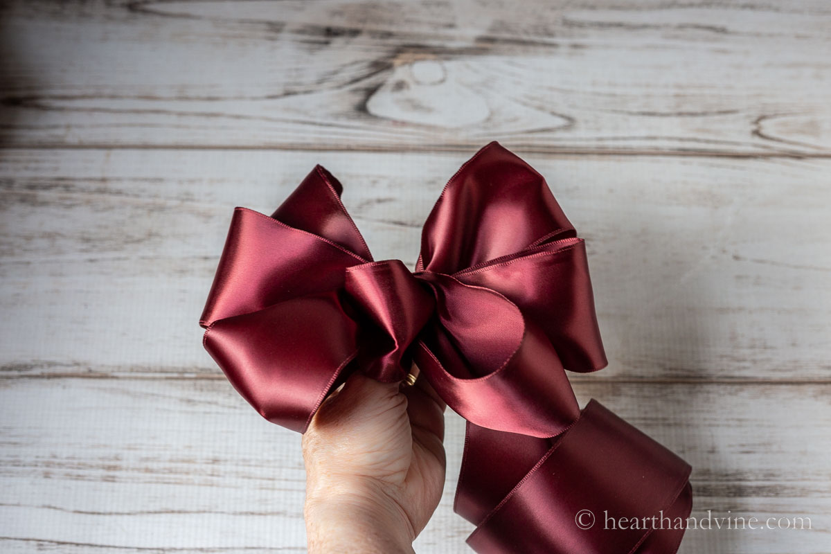 A hand hold a red bow made from ribbon.