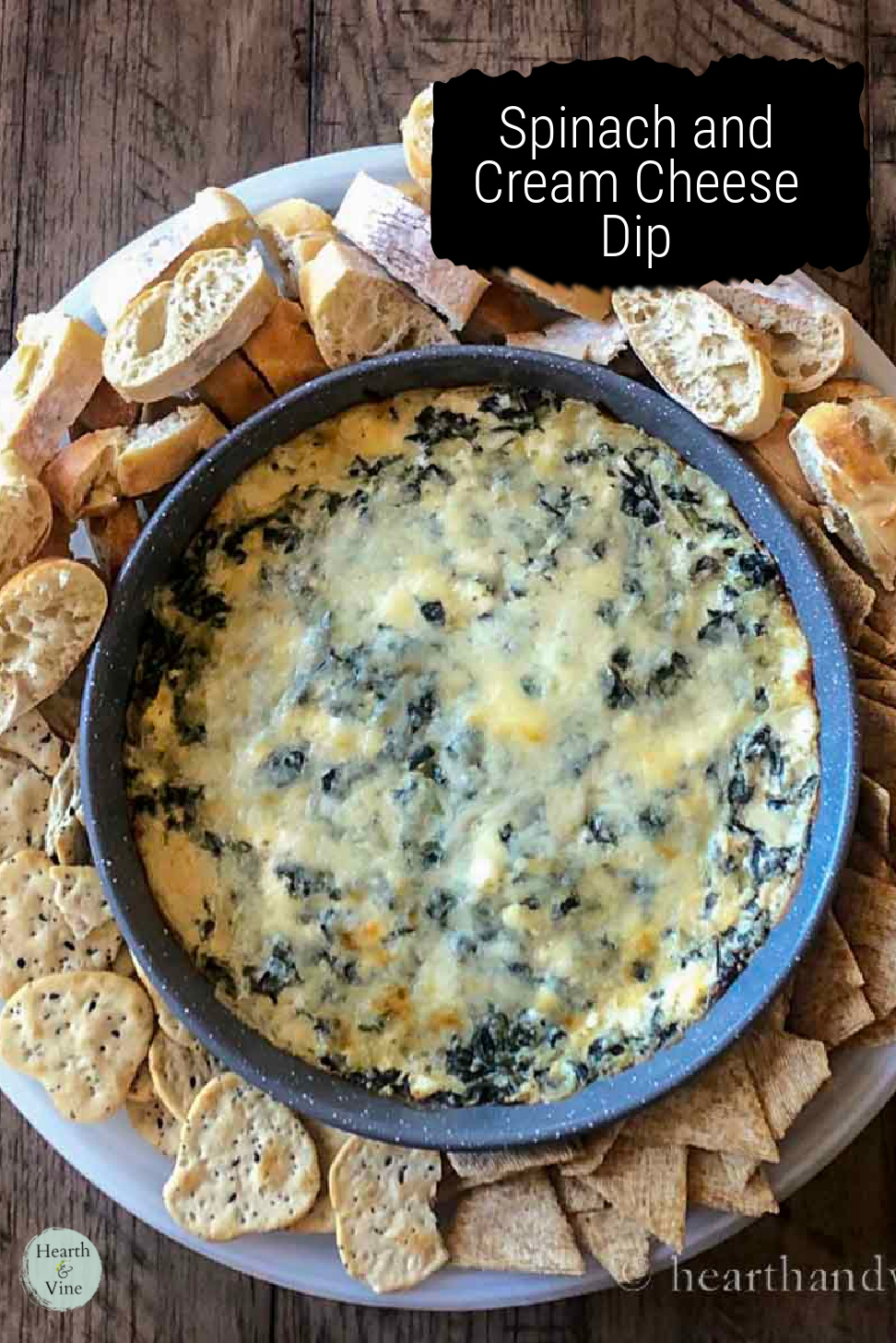 Aerial view of baked spinach dip with sliced bread and crackers.