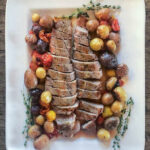 Sheet pan pork tenderloin sliced on a platter with potatoes and tomatoes