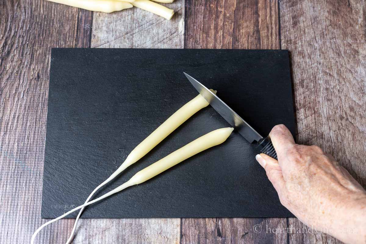 A set of hand dipped candles on slate and a knife cutting the ends.