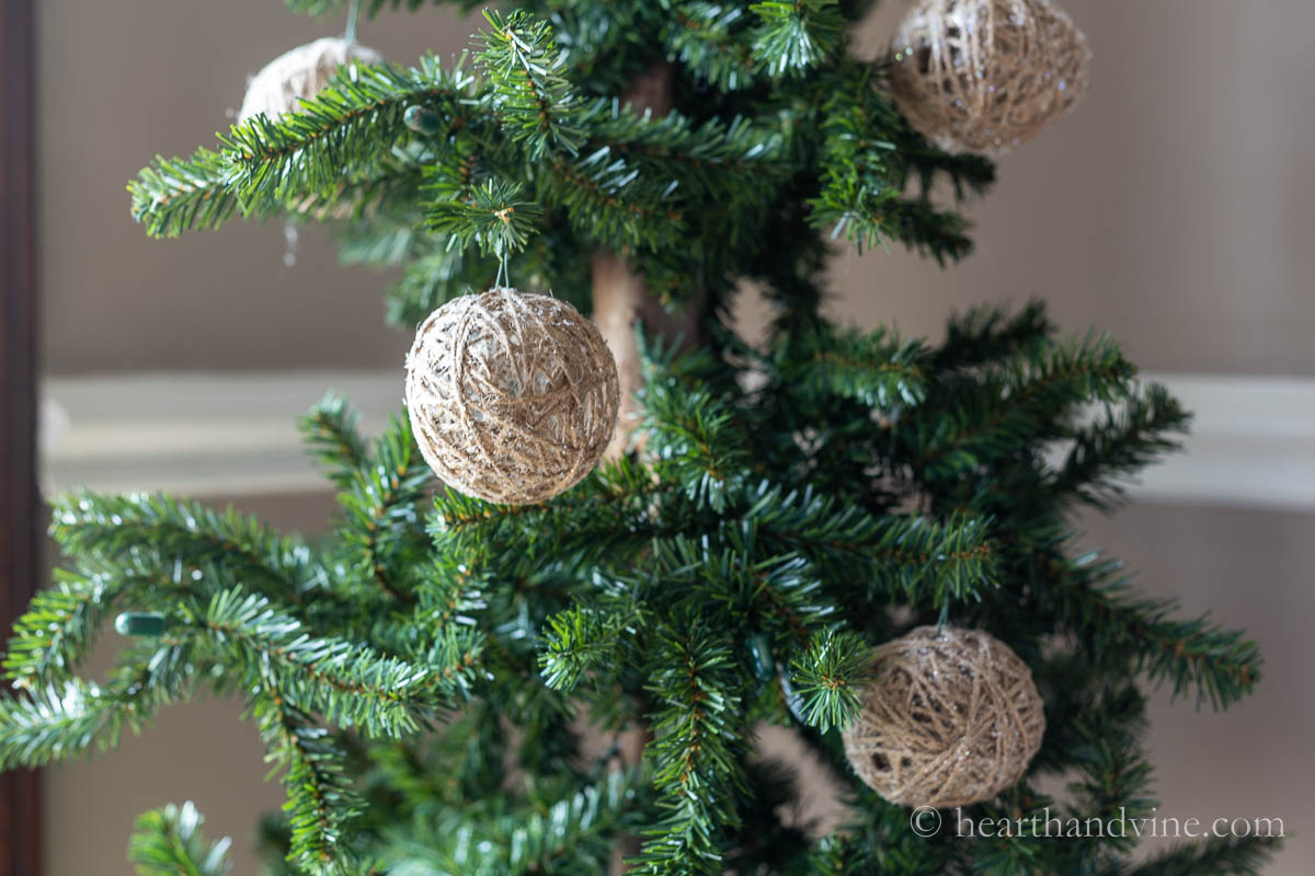Several twine ball ornaments hanging on a Christmas tree.