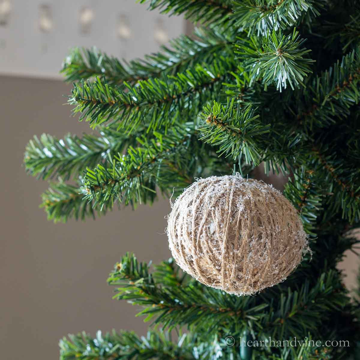 I glittered twine ball ornament hanging on a Christmas tree.