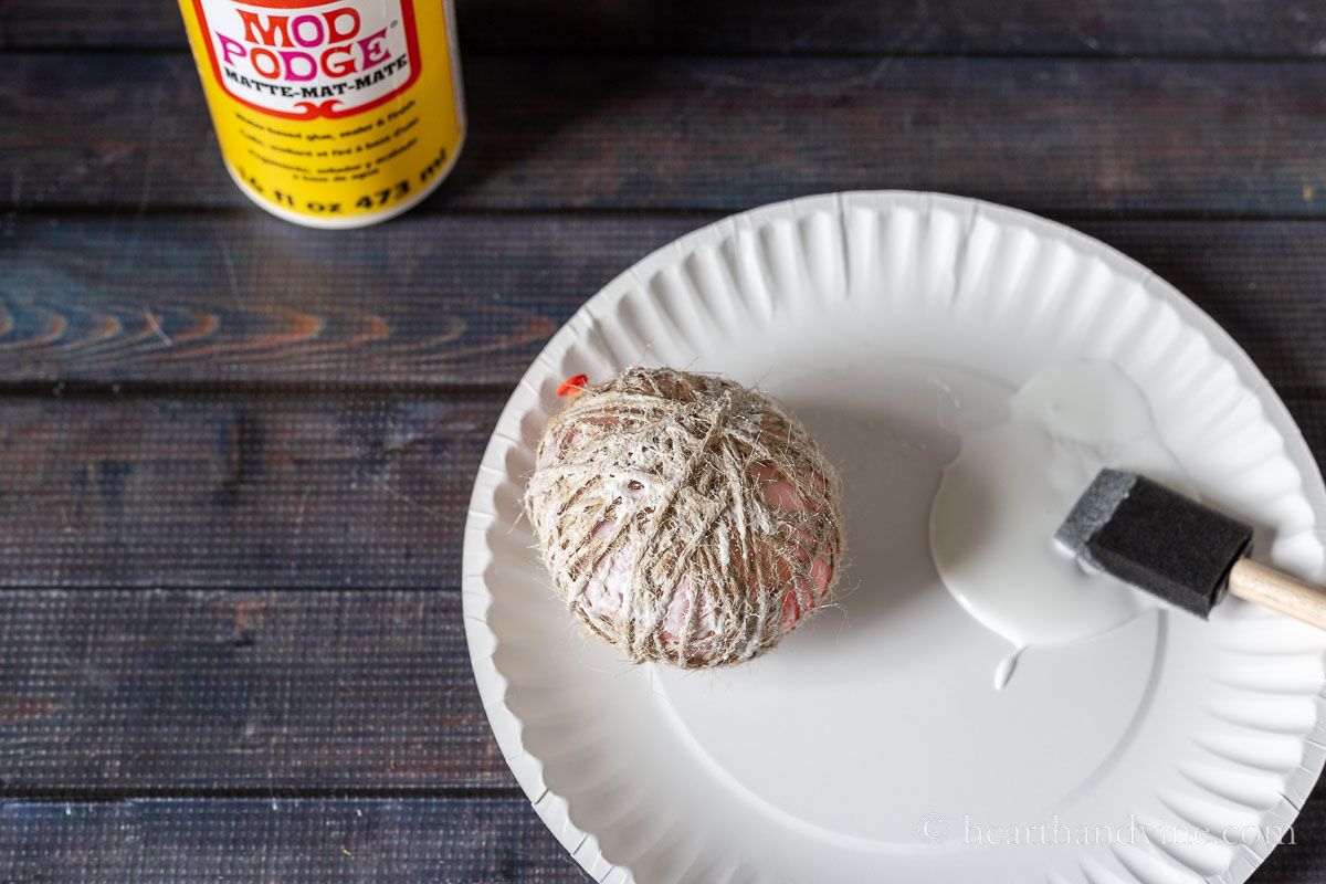 A balloon wrapped in twine next to a sponge brush and a some Mod Podge.