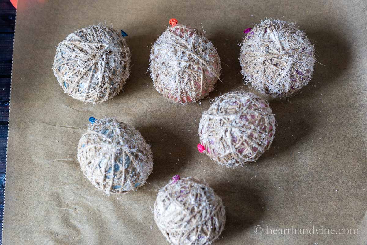 Several twine covered balloons with glue and glitter on a piece of parchment paper.