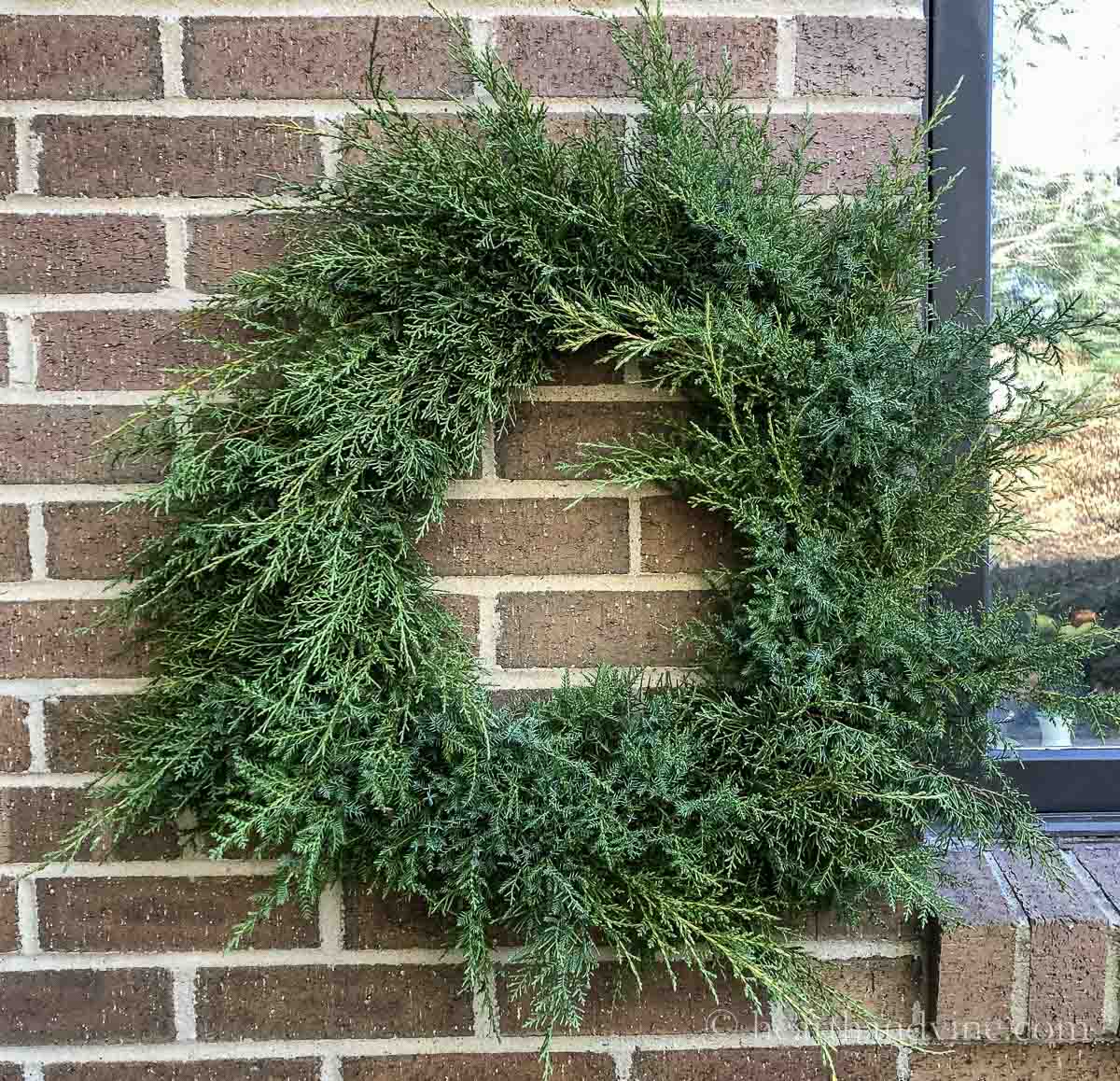 A fresh juniper wreath hanging on a brick wall.