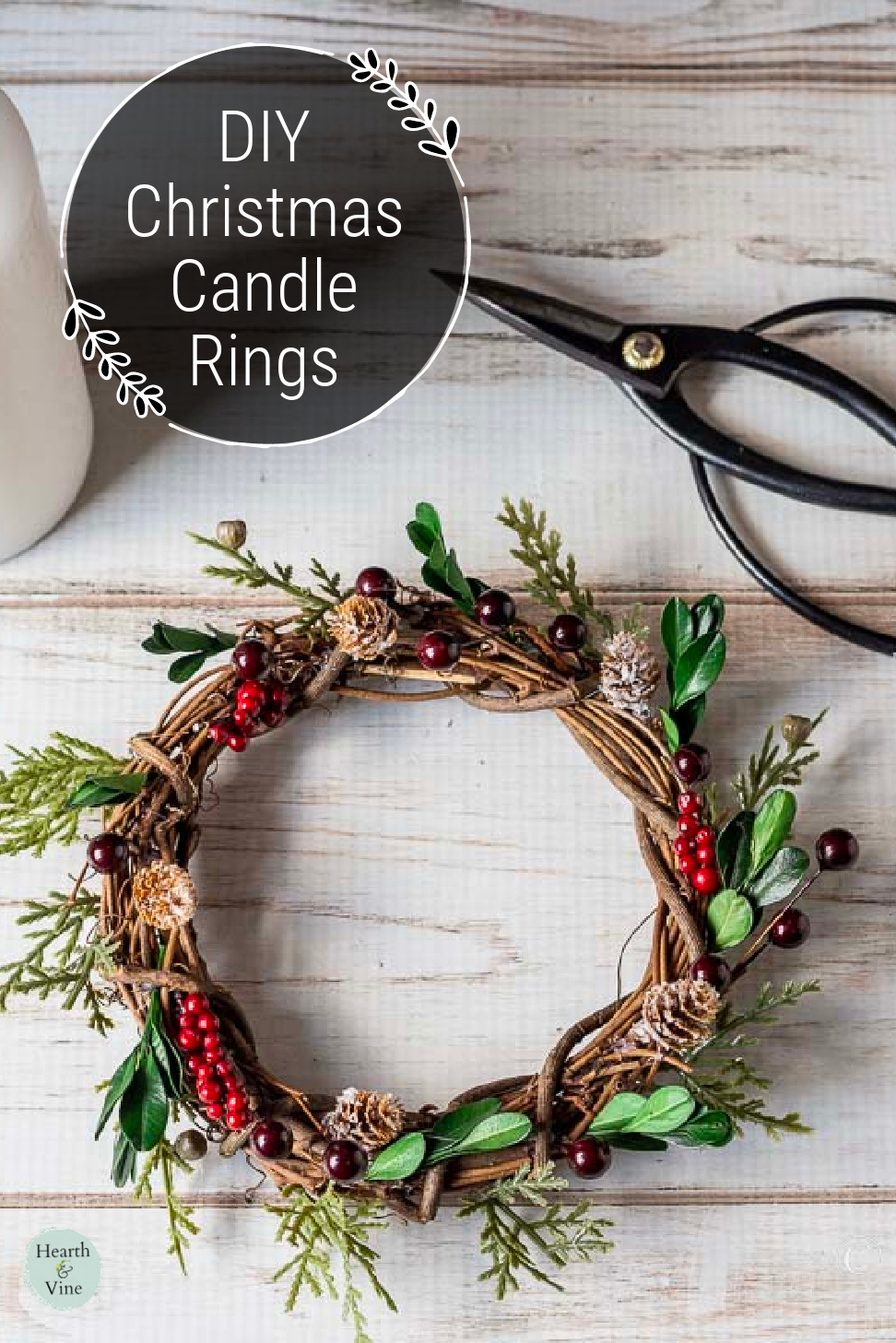 A holiday themed candle wreath with scissors and a pillar candle on the side.