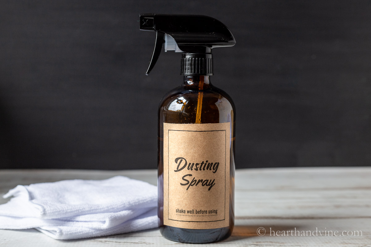 A DIY dusting spray bottle with a kraft label next to a white microfiber cloth.