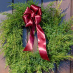 Red bow on a green wreath hanging on a front door.