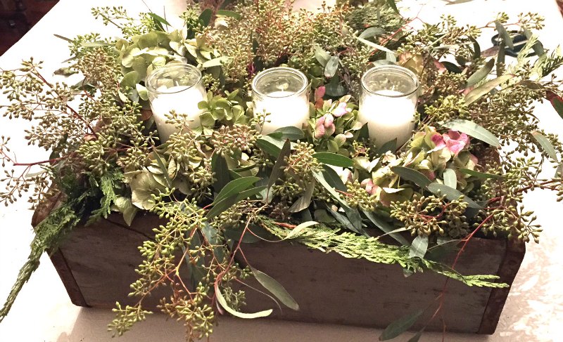 Wooden box with candles, dried hydrangea flowers, cedar greenery and seeded eucalyptus berries.