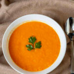 White bowl of sweet potato carrot ginger soup with parsley.