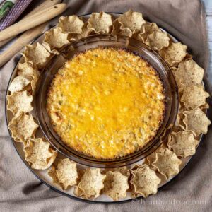 Corn dip with cream cheese in a pie plate with tortilla scoops all around.