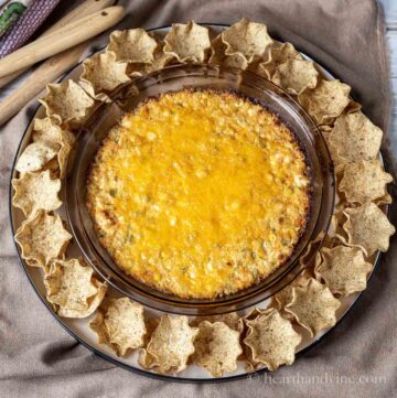 Corn dip with cream cheese in a pie plate with tortilla scoops all around.