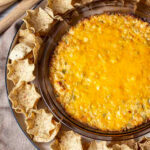 Partial view of baked hot corn dip with wheat scoop tortilla chips around the edges.