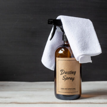Amber bottle of DIY dusting spray with white microfiber cloth on top.