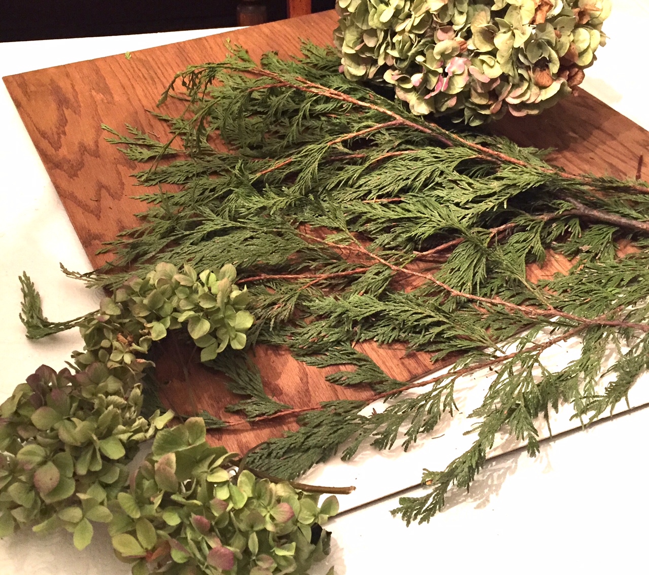 Pieces of fresh cedar branches and dried hydrangea blooms on a table.