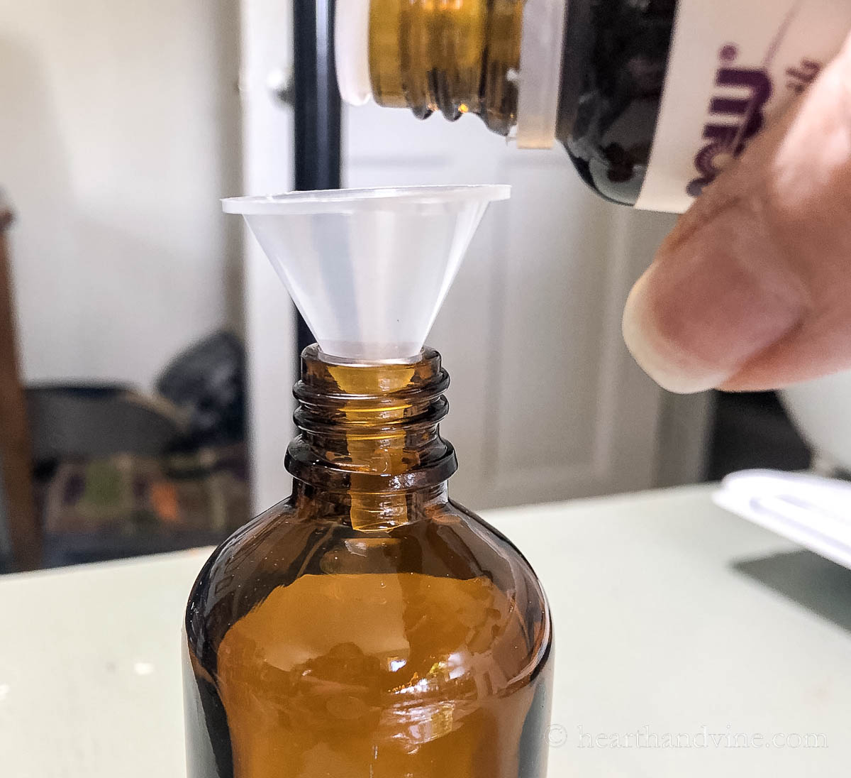 A mini funnel in an amber glass bottle with a bottle of essential oil pouring into it.
