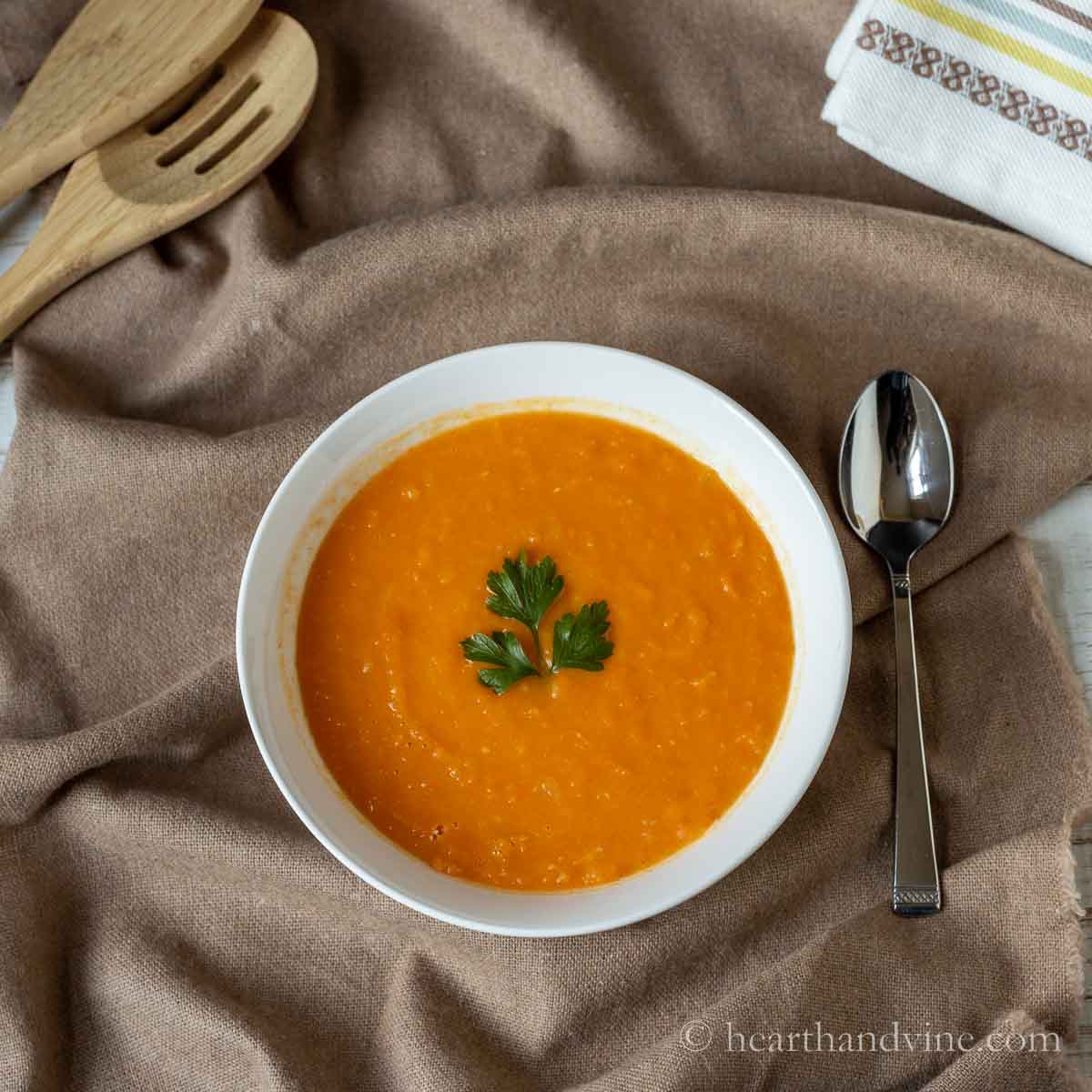 Bowl of sweet potato and carrot soup with a sprig of parsley.