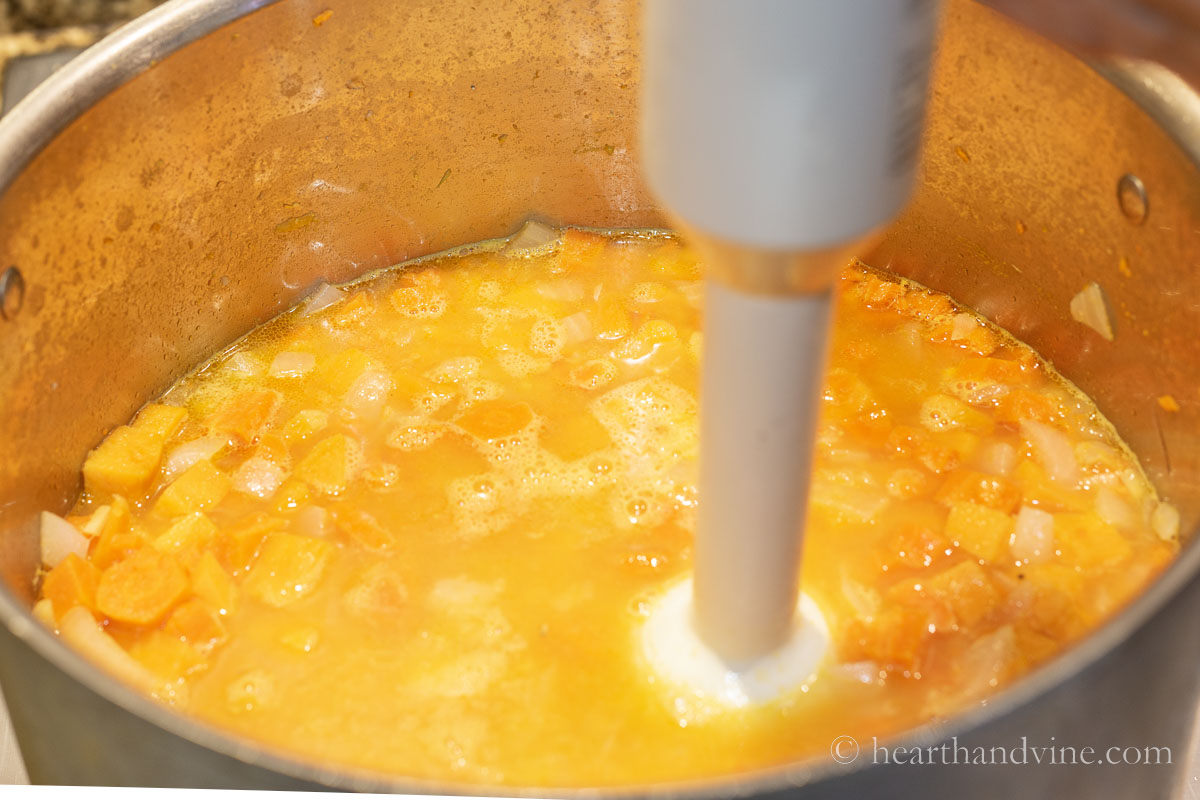 An immersion blender pureeing the sweet potato and carrot soup.