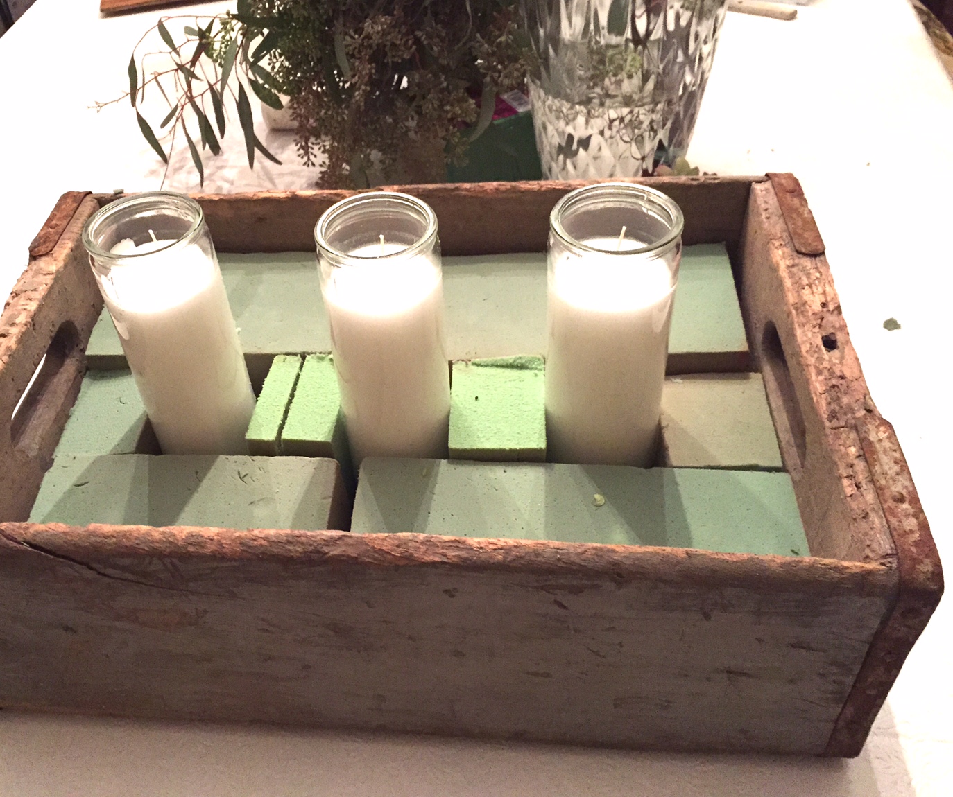 Antique box with floral foam and three glass candles.