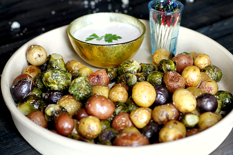 Brussel sprouts and mini potatoes in a serving dish with a small bowl of blue cheese dip and some toothpicks.